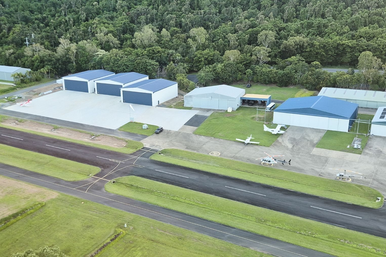 Aerial view of three custom aircraft hangars beside the runway at Whitsunday Airport, Shute Harbour near Airlie Beach QLD, designed and constructed by Entegra